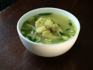 Photograph: white bowl of clear fish soup with herbs on wooden table