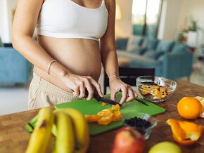 Pregnant woman cutting some vegetable in a cutting board