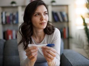 Photograph of a pensive woman on a sofa holding a pregnancy test