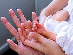 Mão adulta a segurar a mão minúscula de um bebé prematuro, contraste de tamanhos, sem mostrar rostos