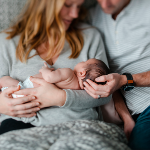 Photograph: parents tenderly hold two newborns on a gray blanket