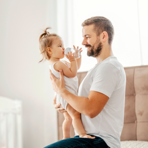 Photograph: smiling father holding waving toddler daughter in bright nursery