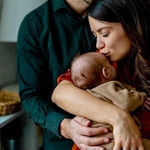 Um casal segura carinhosamente um bebé adormecido dentro de casa