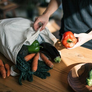 Photo of hands unpacking reusable bag with carrots, eggplant, greens, red bell pepper