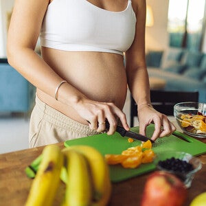 Pregnant woman cutting some vegetable in a cutting board