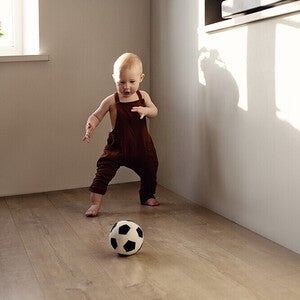 Photograph: barefoot toddler in burgundy romper kicking soccer ball on wooden floor
