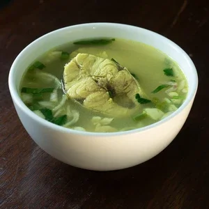 Photograph: white bowl of clear fish soup with herbs on wooden table