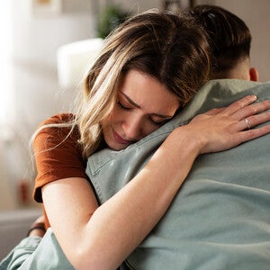 Photograph: woman with eyes closed receiving a comforting hug on a couch