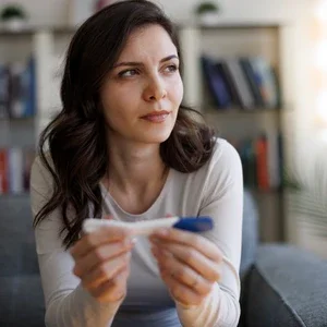 Photograph of a pensive woman on a sofa holding a pregnancy test