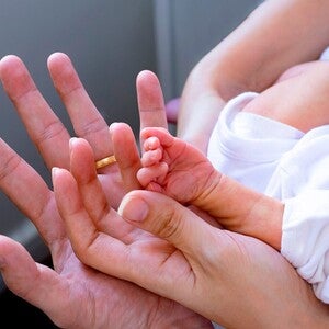 Mão adulta a segurar a mão minúscula de um bebé prematuro, contraste de tamanhos, sem mostrar rostos