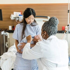 Médica cuidando de bebê no colo da mãe em ambiente hospitalar.