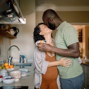 Casal se abraça na cozinha, com afeto e alegria, perto de uma bancada com frutas.