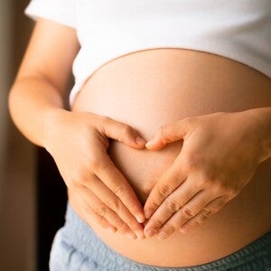 Mulher grávida formando coração com mãos na barriga.