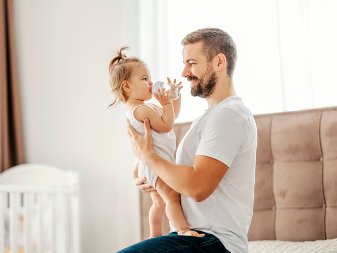 Photograph: smiling father holding waving toddler daughter in bright nursery