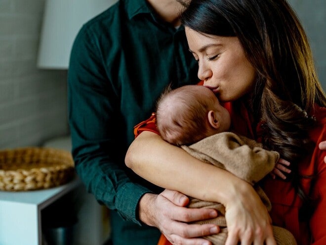 Um casal segura carinhosamente um bebé adormecido dentro de casa