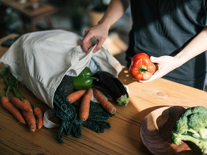 Photo of hands unpacking reusable bag with carrots, eggplant, greens, red bell pepper