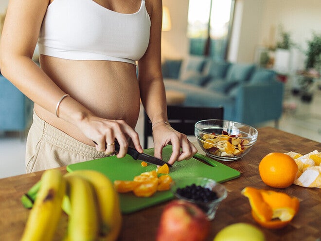 Pregnant woman cutting some vegetable in a cutting board