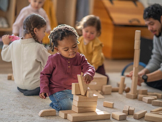 Photograph of children and teacher building with wooden blocks in a warm playroom