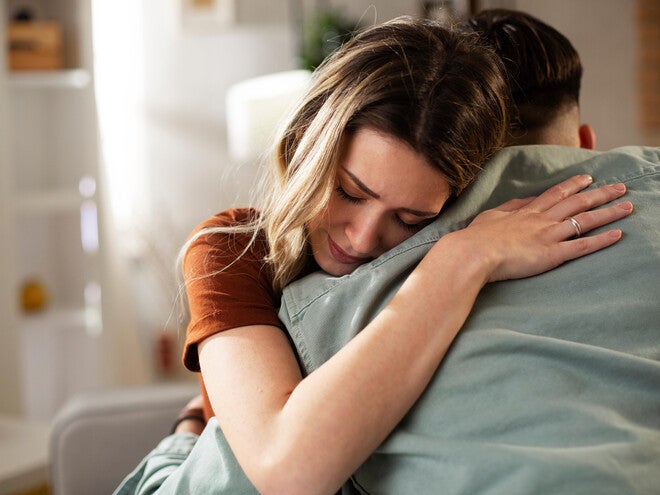 Photograph: woman with eyes closed receiving a comforting hug on a couch