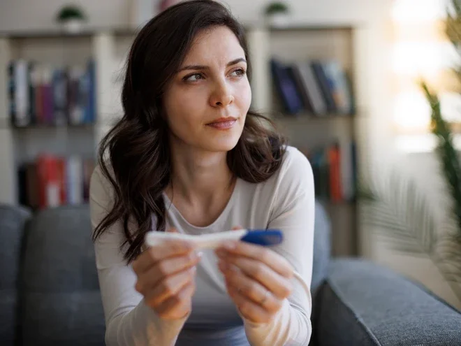 Photograph of a pensive woman on a sofa holding a pregnancy test