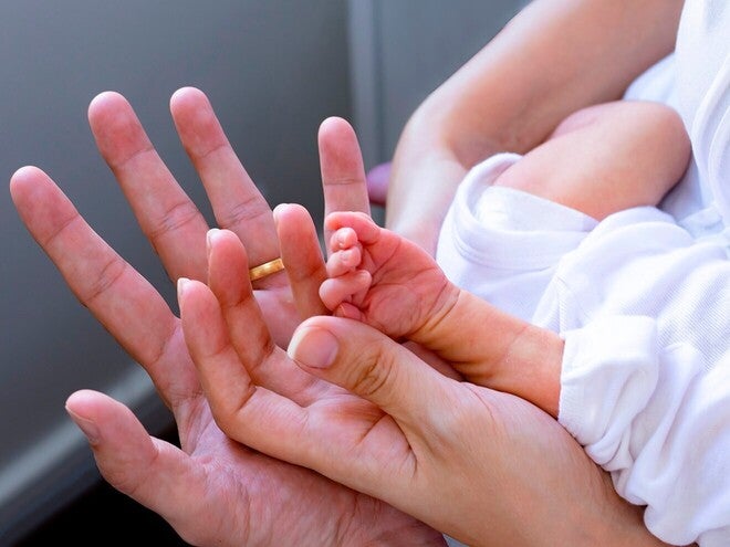 Mão adulta a segurar a mão minúscula de um bebé prematuro, contraste de tamanhos, sem mostrar rostos