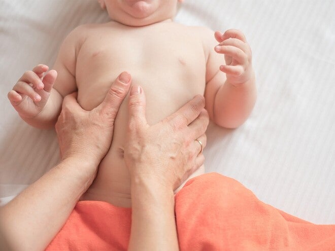 Mão de adulto a fazer massagem suave em barriga de bebé deitado sobre uma manta de algodão