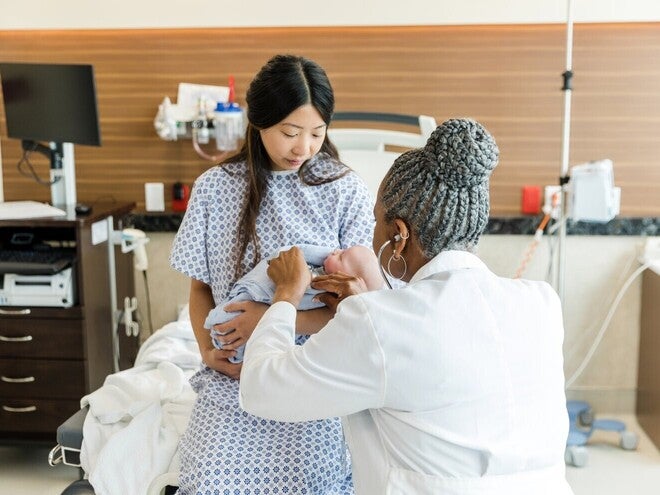 Médica cuidando de bebê no colo da mãe em ambiente hospitalar.