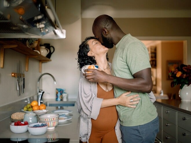Casal se abraça na cozinha, com afeto e alegria, perto de uma bancada com frutas.