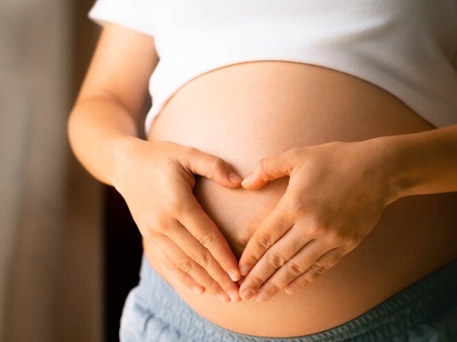 Mulher grávida formando coração com mãos na barriga.