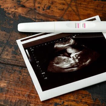 White pregnancy test showing two pink lines beside an ultrasound photograph on wooden table