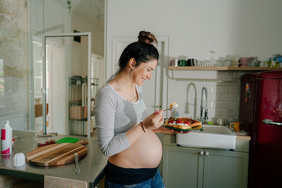 Photograph: pregnant woman smiling in kitchen holding a bowl of salad.