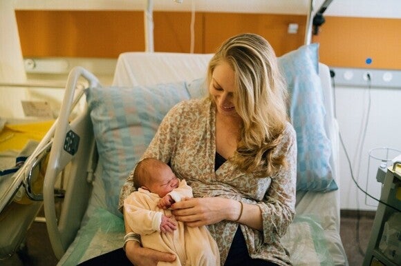 Fotografia de uma mãe recente numa cama hospitalar, embalando o seu recém-nascido envolto em panos.