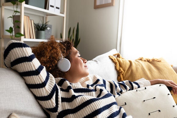 Photograph of a relaxed young person with curly hair wearing headphones on a sunlit couch